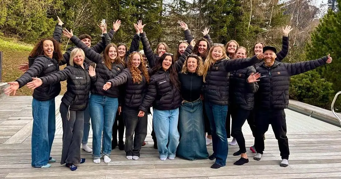 The Alpine Shine team together on a chalet deck in M&eacute;ribel, arms outstretched in branded jackets with the mountains behind them