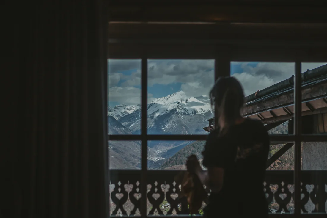 An Alpine Shine team member by a chalet window overlooking the snowy mountains